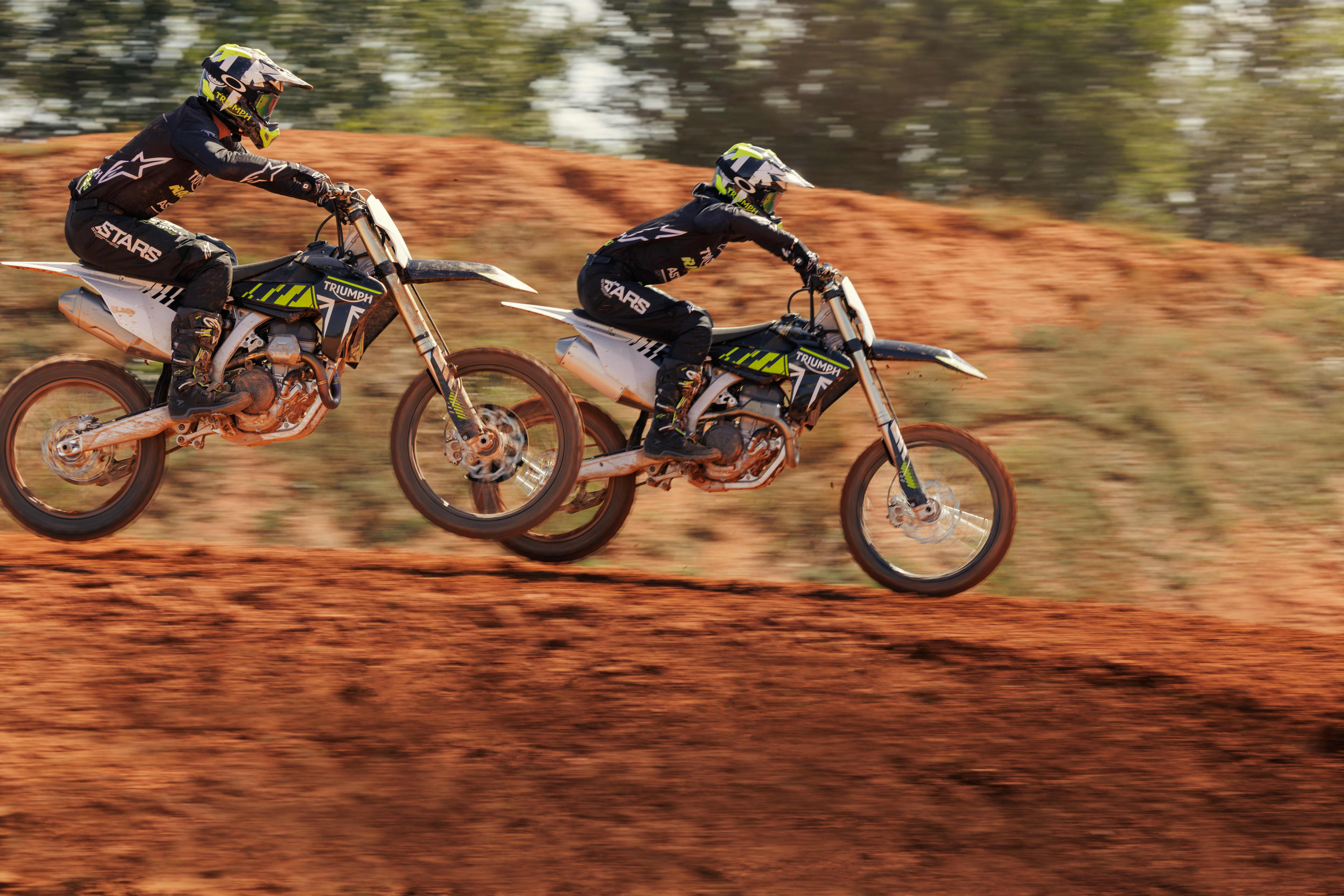 Side view of two riders on Triumph TF 250-X (MY24) bikes racing on a motocross track
